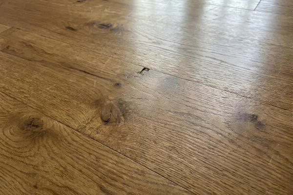 Worn hardwood flooring with visible scratches, scuffs, knots, and surface damage.